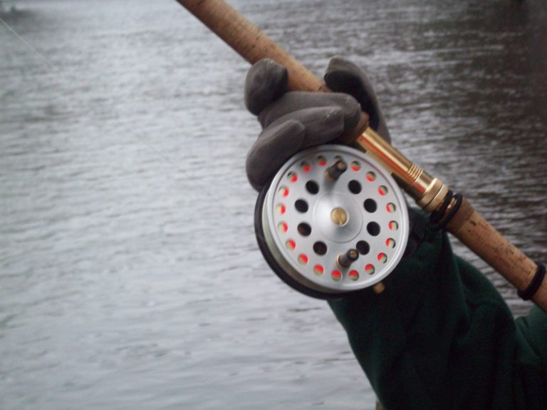 Center pin reel being held by angler wearing gloves.