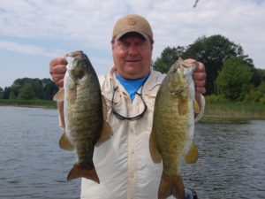 man holds up two fish caught while bass fishing on the St. Lawrence River.