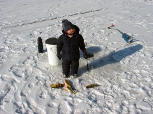 young boy stands next to an ice fishing hole in the central Lake Ontario region. 