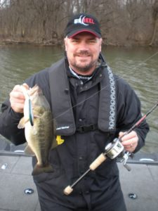 Angler holding a largemouth bass on a boat while ice out bass fishing on Lake Ontario.