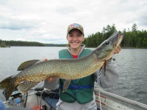 young girl on a boat posing with a large northern pike.