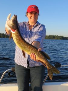 woman on a lake in a boat holding a northern pike