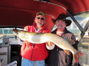 two men on a boat holding a large northern pike