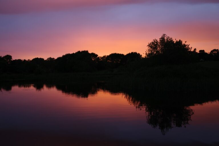 The sun fully sets on a lake.