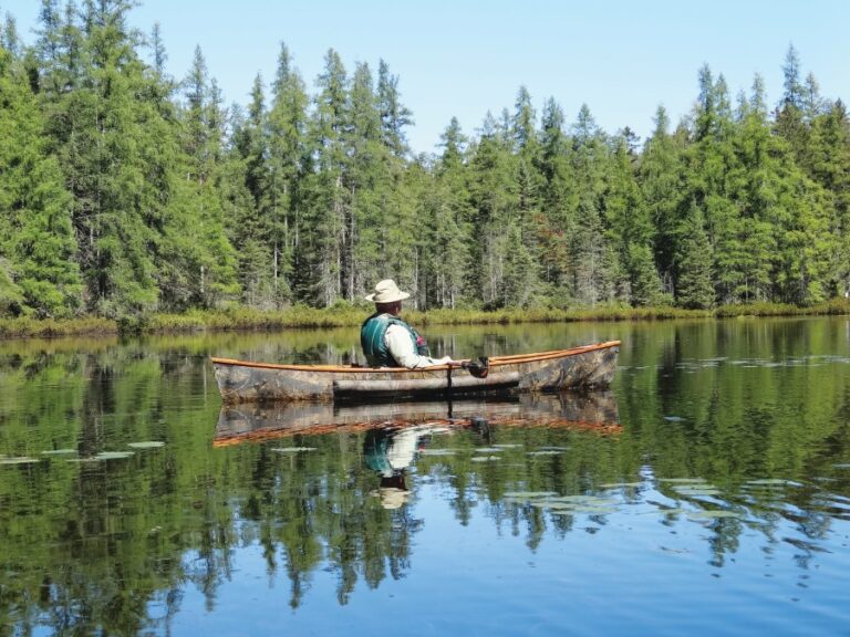Fisherman sits inside of a canoe covered in camouflage.