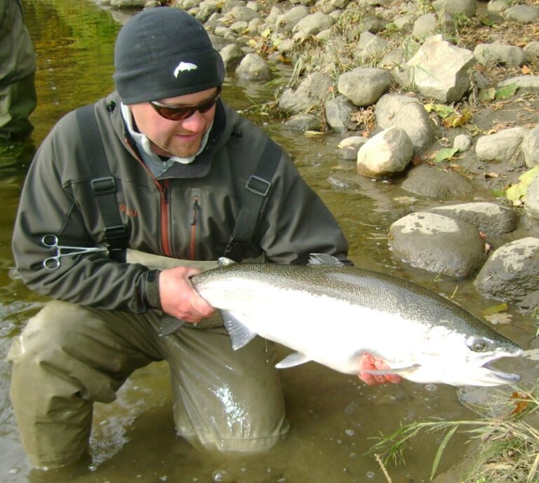 Angler holds up a large steelhead caught on a float.